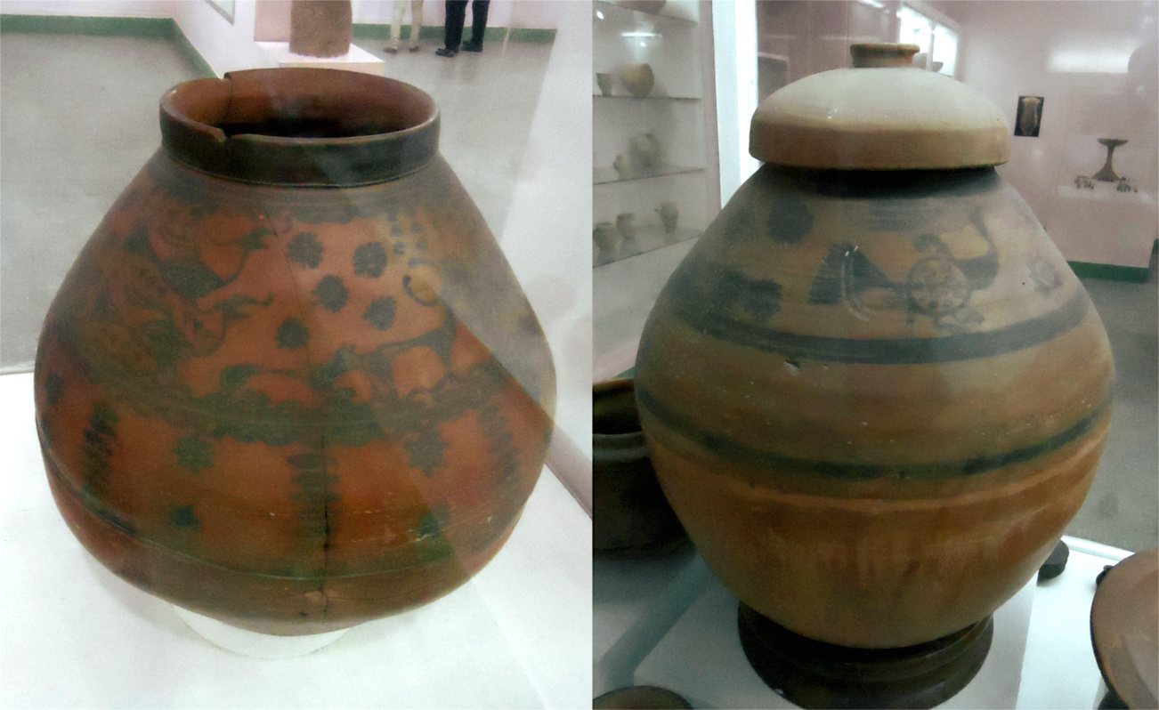 Two round painted pottery jars in a museum case, decorated in dark bands with dotted and animal motifs