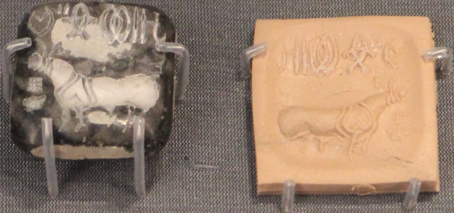A small square seal of dark stone beside its pale modern impression, showing a bull without a hump beneath a row of signs