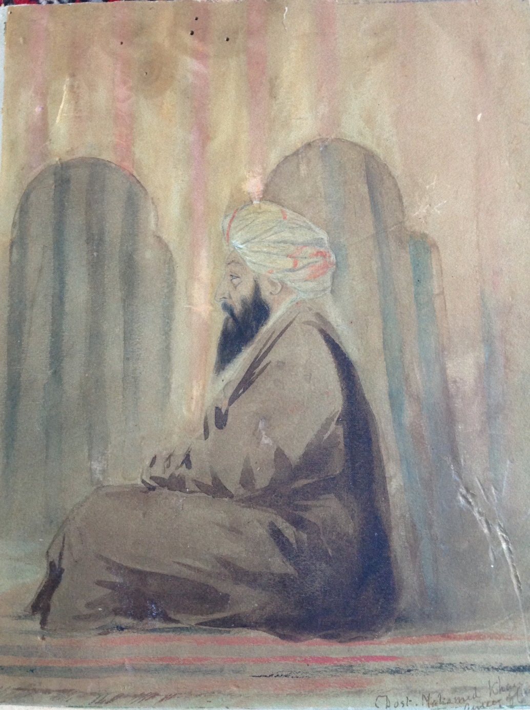 Watercolour of a bearded man in a white turban and a loose brown robe, seated cross-legged in profile before two arched niches, with a handwritten name in the lower corner.