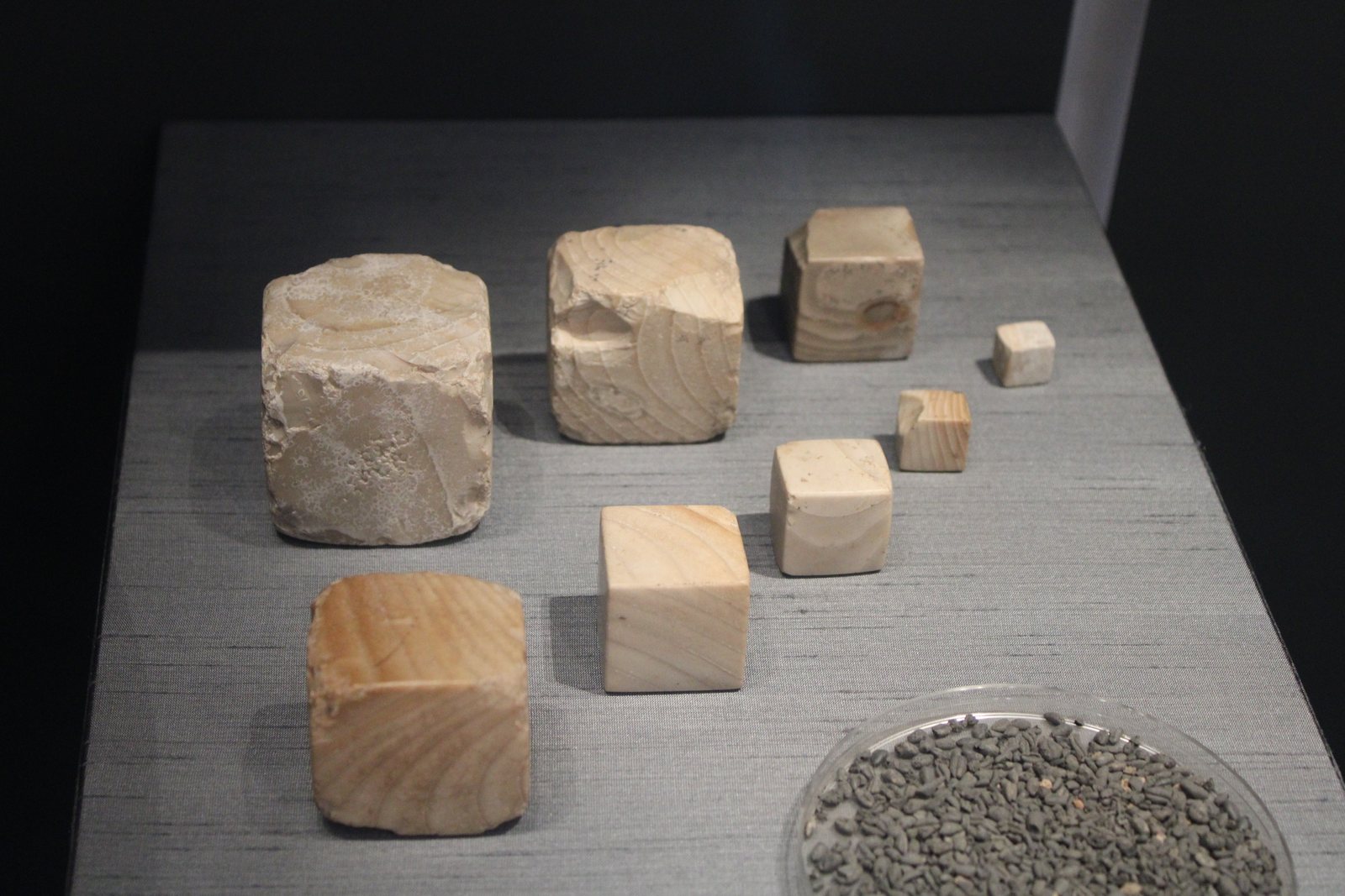 Eight pale stone cubes of graded sizes, from large to very small, displayed in a museum case
