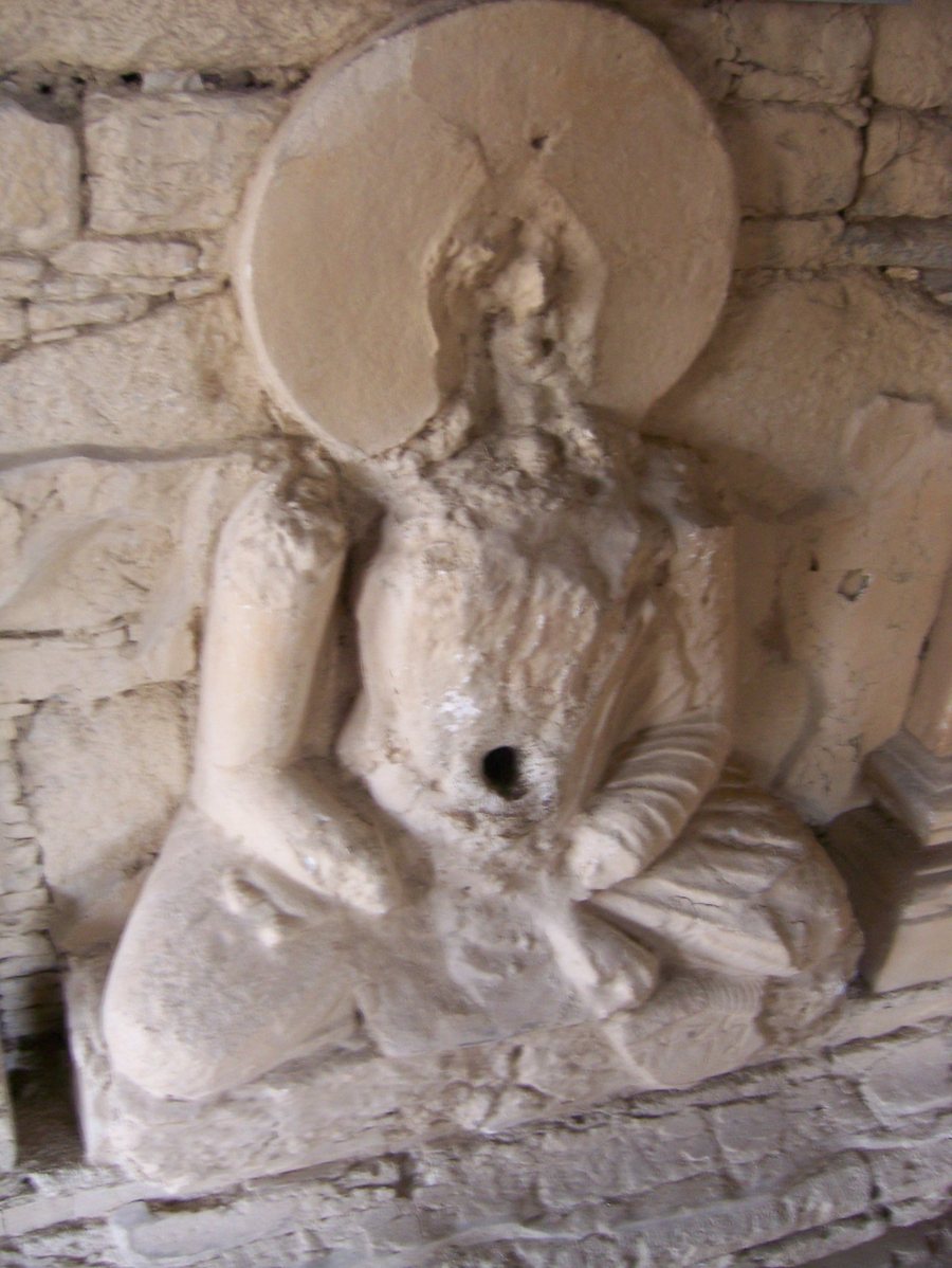 A worn white stucco seated Buddha in a niche, the face and halo damaged, with a small round hole at the navel