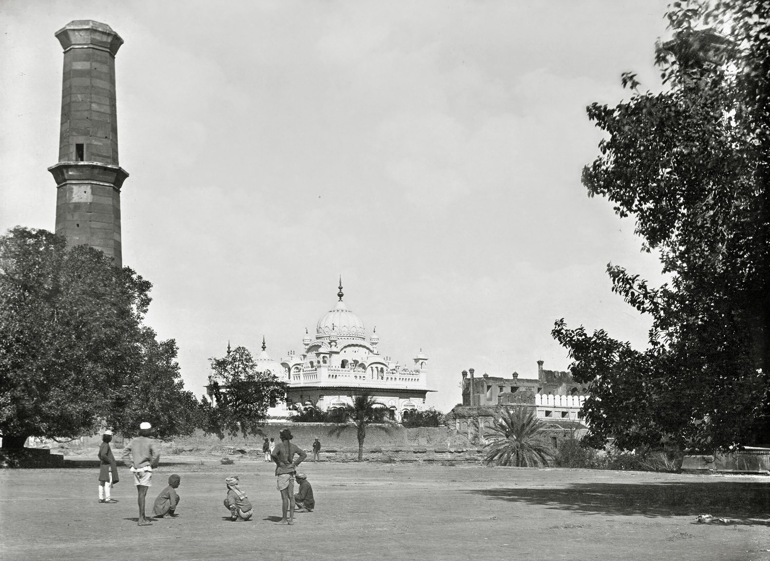 Nineteenth-century photograph: a tall, plain minaret without its top stands on the left, and across an open square the white domes of the samadh of Ranjit Singh rise behind a wall, with men and boys standing in the foreground.