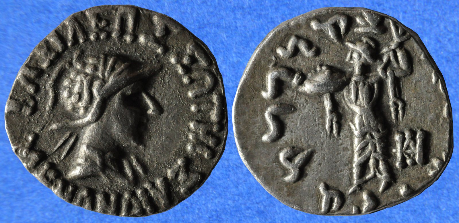 Both faces of a small silver coin: a king's head in a crested helmet ringed by Greek letters, and a standing armed goddess with a shield ringed by Kharosthi letters