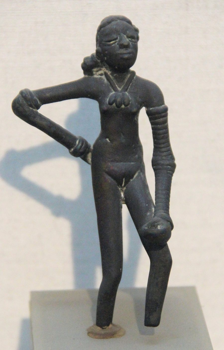 A small dark bronze figurine of a standing woman, one hand on her hip, her left arm covered in bangles from wrist to shoulder