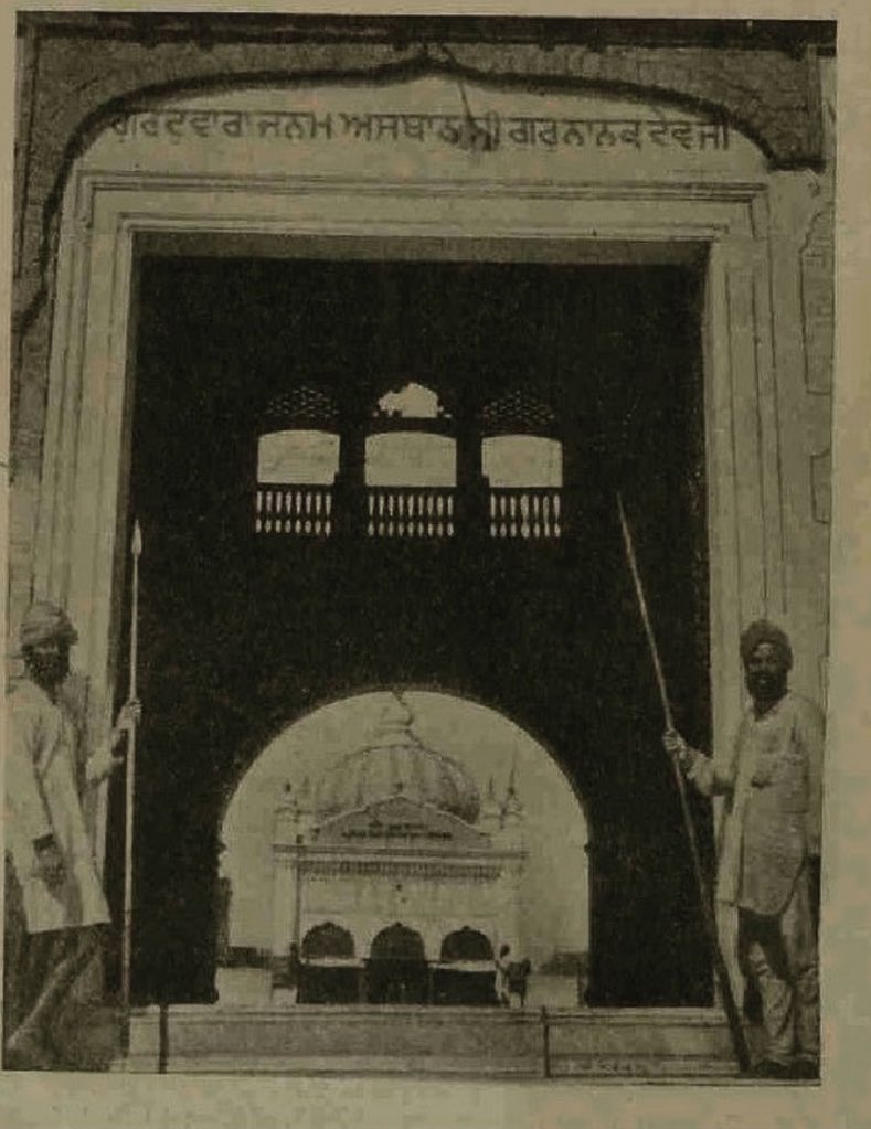 An arched gateway with Gurmukhi lettering above it; two Sikh men with spears stand on either side, and a domed building is visible through the arch