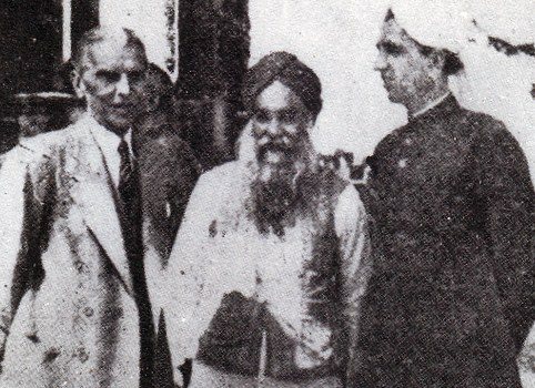 Three men standing together: on the left a tall man in a pale suit, in the centre a bearded Sikh in a turban, on the right a man in a dark high-collared coat