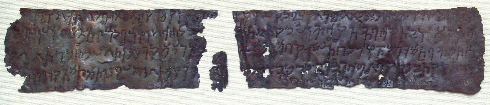 A long, thin copper plate broken into two large pieces and a small one, its surface covered with rows of dotted Kharosthi letters
