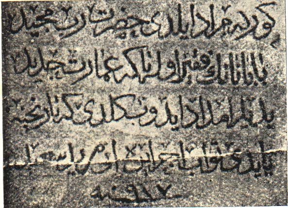 A grainy black-and-white photograph of a stone slab carved with four lines of Arabic-script writing and a short line beneath