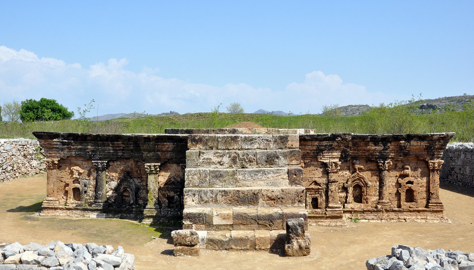 The stone base of a shrine with a central stairway, its front divided by carved pilasters into niches, some with pointed pediments and some with rounded arches